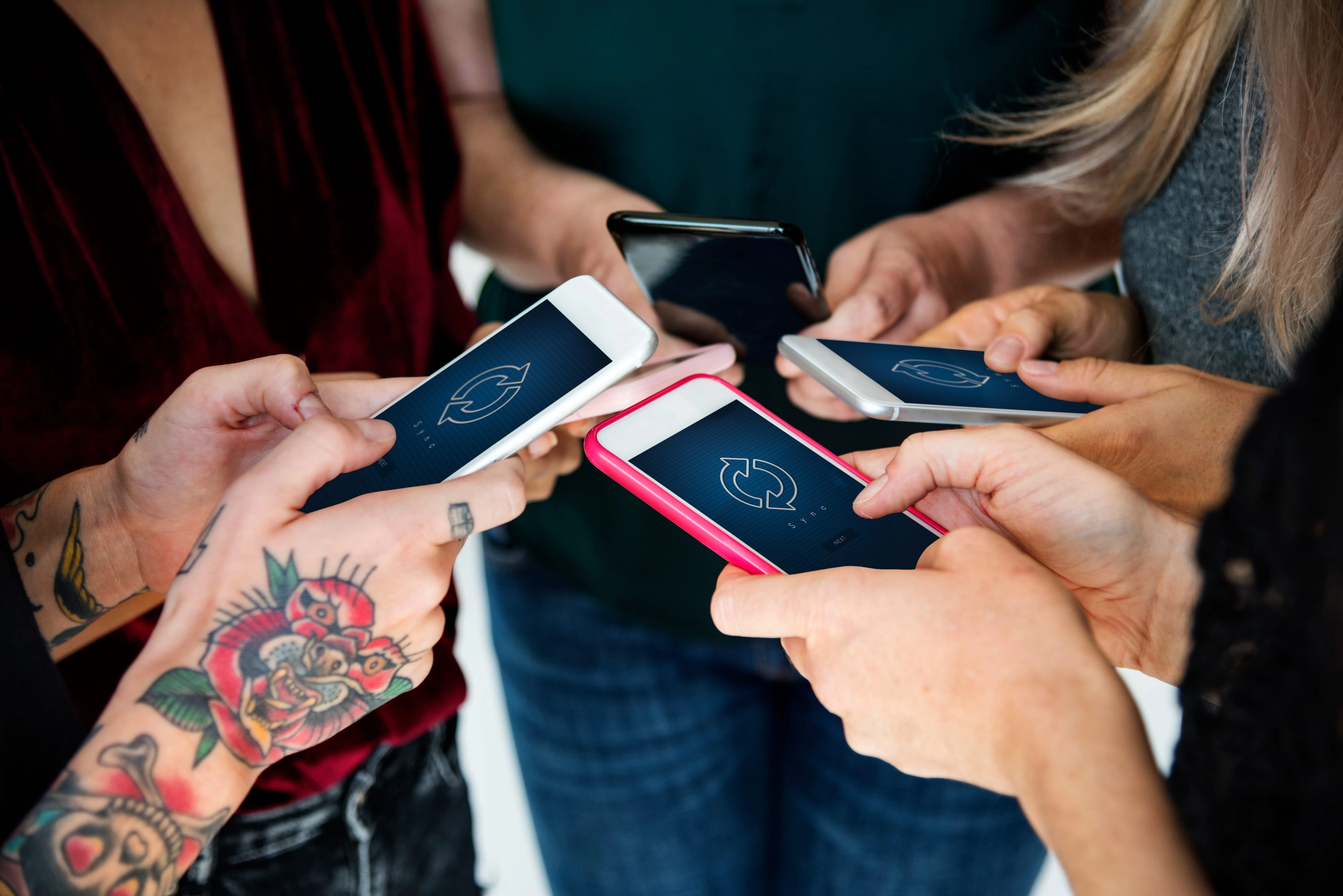 Mehrere Hände halten Smartphones mit Sync-Symbol dicht beieinander
