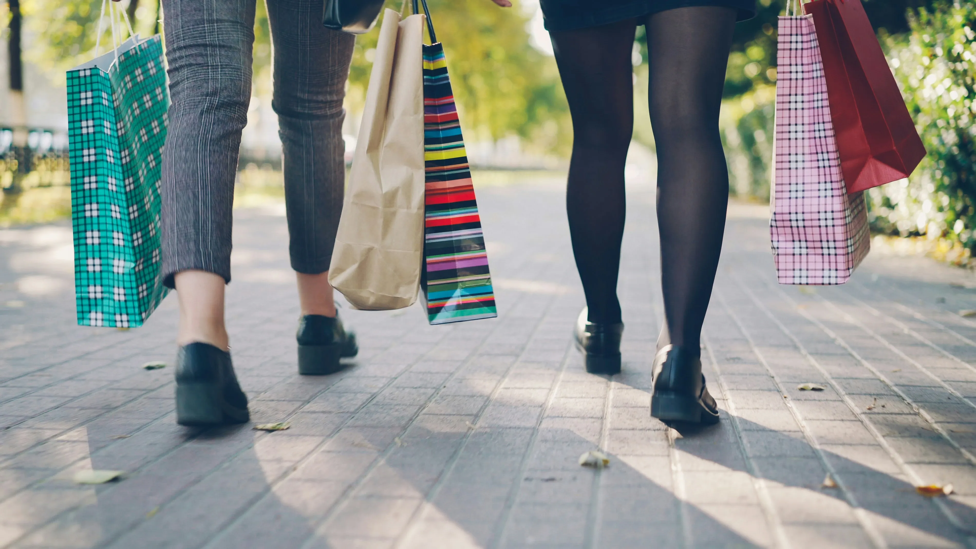 Zwei Kundinnen gehen mit bunten Einkaufstüten die Straße entlang